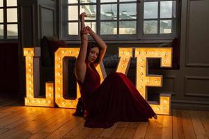 Woman in red dress making letter V in front of LOVE letters photo