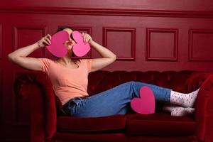 Women with lips shaping kiss on couch holding heart shapes in front of her face photo