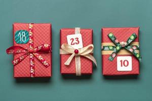 cajas de regalo rojas y verdes envueltas a mano decoradas con cintas, copos de nieve y números, adornos navideños y decoración en la mesa verde concepto de calendario de adviento de navidad vista superior tarjeta de vacaciones plana foto