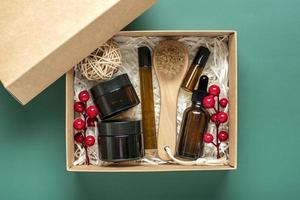 Set for care box Eco-friendly cosmetics Oil and cream bottles, brush for washing, cotton pads on green background Gift for girlfriend, mother to celebrate Christmas concept Top view Flat lay photo