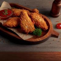 Crispy fried chicken on a wooden plate with tomato sauce