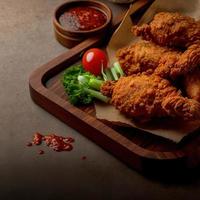 Crispy fried chicken on a wooden plate with tomato sauce photo