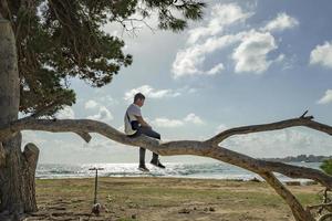 teenager climbing a tree against the blue sky in front of the sea photo