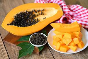 frutas de papaya sobre fondo de madera, rodajas de papaya maduras frescas en un plato de frutas tropicales con semillas de papaya y hojas de árbol de papaya foto