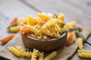 Pasta raw macaroni on wooden bowl background, close up raw macaroni spiral pasta uncooked delicious whole grain fusilli pasta for cooking food photo