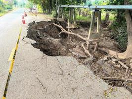 Asphalt road collapsed and cracks in the roadside, Road landslide subside with road cone caused by river erosion photo