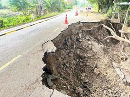 Asphalt road collapsed and cracks in the roadside, Road landslide subside with road cone caused by river erosion photo