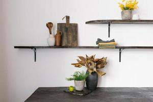 A bouquet of dried flowers and a green plant on the background of the interior of a modern kitchen in the Scandinavian style. Kitchen utensils on a wooden shelf cutting board photo