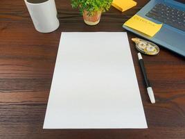 Flat lay, mock up paper. workspace in the background of the office desk from the top view.  with blank white paper, laptops, office supplies, pencils, green leaves, and coffee cups in a wooden table. photo