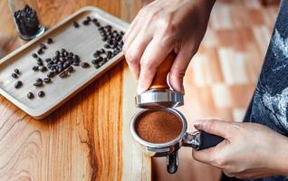 Barista cafe making coffee with manual presses ground coffee using tamper on the wooden counter bar at the coffee shop photo