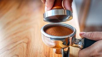 Close-up of hand Barista cafe making coffee with manual presses ground coffee using tamper on the wooden counter bar at the coffee shop photo