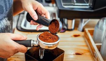 Barista pours coffee bean roaster powder ground coffee pouring into a portafilter with a barista hand at the coffee shop photo