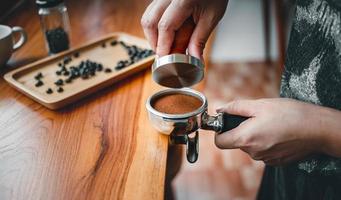 Barista cafe making coffee with manual presses ground coffee using tamper on the wooden counter bar at the coffee shop photo