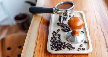 equipo de manipulación de herramientas de café barista y café templado en granos de café tostados de portafiltro sobre mesa de madera foto