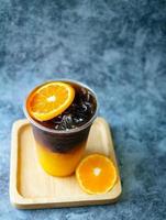 menú de bebida de café helado fusión de naranja americano con fruta fresca de naranja mezclada en una taza de plástico, producto de menú de bebida. foto