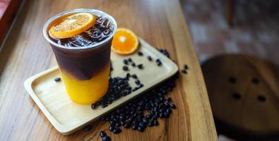 menú de bebidas de café helado naranja americano con fruta fresca de naranja mezclada en un vaso de plástico en el mostrador de madera de la cafetería foto