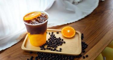 menú de bebidas de café helado naranja americano con fruta fresca de naranja mezclada en un vaso de plástico en el mostrador de madera de la cafetería foto