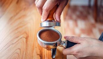 Close-up of hand Barista cafe making coffee with manual presses ground coffee using tamper on the wooden counter bar at the coffee shop photo