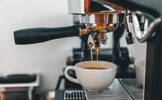 Coffee extraction from the coffee machine with a portafilter pouring coffee into a cup,Espresso poruing from coffee machine at coffee shop photo