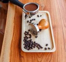 equipo de manipulación de herramientas de café barista y café templado en granos de café tostados de portafiltro sobre mesa de madera foto