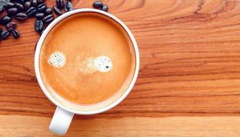 taza blanca de café espresso y granos de café tostados sobre un fondo de madera foto