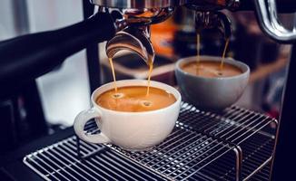 extracción de café de la máquina de café con un portafiltro que vierte café en una taza, espresso de la máquina de café en la cafetería foto