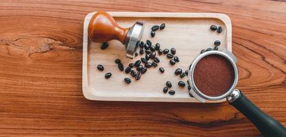 equipo de manipulación de herramientas de café barista y café templado en granos de café tostados de portafiltro sobre mesa de madera foto