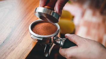 Close-up of hand Barista cafe making coffee with manual presses ground coffee using tamper on the wooden counter bar at the coffee shop photo