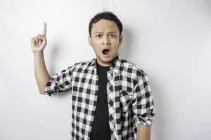 Shocked Asian man wearing tartan shirt pointing at the copy space on top of him, isolated by a white background photo