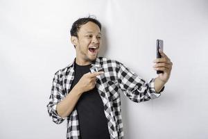 un retrato de un hombre asiático feliz sonríe mientras sostiene su teléfono, aislado por fondo blanco foto