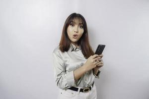 Shocked Asian woman wearing sage green shirt and holding her phone, isolated by white background photo