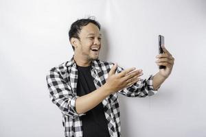 un retrato de un hombre asiático feliz sonríe mientras sostiene su teléfono, aislado por fondo blanco foto