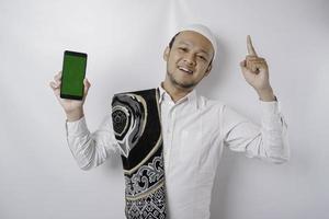 un retrato de un musulmán asiático feliz sonriendo mientras muestra espacio de copia en su teléfono y señala hacia arriba, aislado por fondo blanco foto