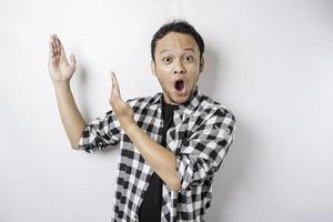 Shocked Asian man wearing tartan shirt pointing at the copy space on top of him, isolated by a white background photo