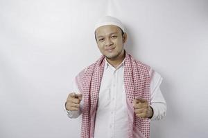 Young Asian Muslim man standing over isolated white background pointing fingers to camera with happy face. Good energy and vibes. photo