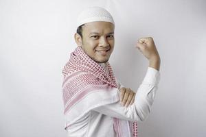 Excited Asian Muslim man showing strong gesture by lifting his arms and muscles smiling proudly photo