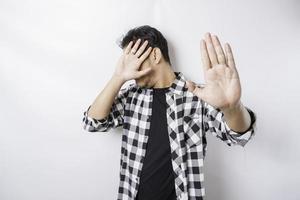 Young scared Asian man isolated on white background, looks depressed, face covered by fingers frightened and nervous. photo