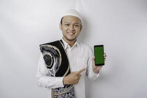 A portrait of a happy Asian Muslim man smiling while showing copy space on his phone, isolated by white background photo