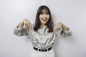 Excited Asian woman wearing sage green shirt pointing at the copy space below her, isolated by white background photo