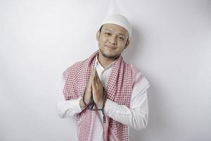 Smiling young Asian Muslim man, gesturing traditional greeting isolated over white background photo