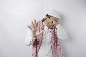 joven musulmán asiático aislado de fondo blanco, se ve deprimido, con la cara cubierta por los dedos, asustado y nervioso.