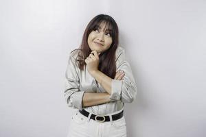 A thoughtful young woman is wearing sage green shirt and holding her chin isolated by white background photo