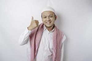 Excited Asian Muslim man gives thumbs up hand gesture of approval, isolated by white background photo