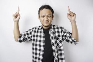 Smiling Asian man wearing tartan shirt is pointing at the copy space on top of him, isolated by white background photo