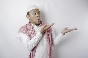 Shocked Asian Muslim man pointing at the copy space beside him, isolated by white background photo