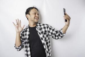 un retrato de un hombre asiático feliz sonríe mientras sostiene su teléfono, aislado por fondo blanco foto