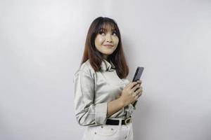 Photo of a thoughtful young woman holding her phone and looking aside. isolated on white color background