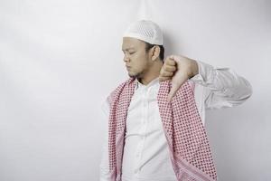 Disappointed Asian Muslim man gives thumbs down hand gesture of approval, isolated by white background photo