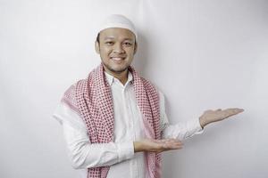 Excited Asian Muslim man pointing at the copy space beside him, isolated by white background photo