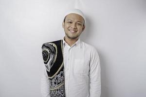 A portrait of a happy Asian Muslim man with prayer rug on his shoulder is smiling isolated by white background photo